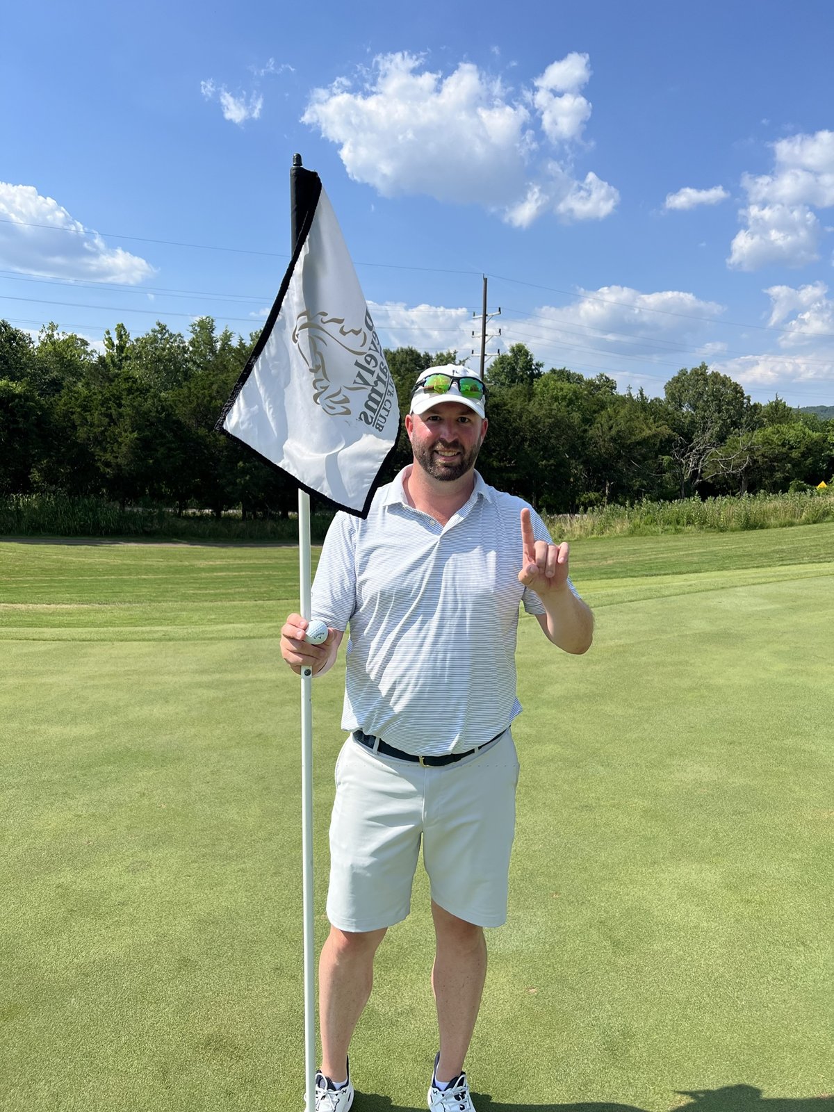 David Mueller on a putting green, holding the flagstick and a golf ball
